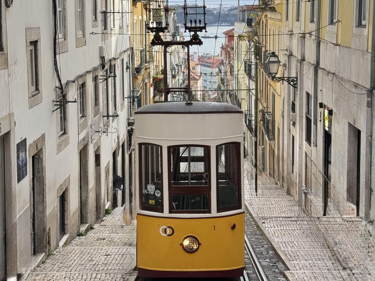 The yellow Bica funicular climbing a steep street in Lisbon, with the river behind